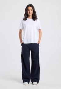 White cotton t-shirt with short sleeves, paired with navy wide-leg sweatpants featuring white side stripes and white sneakers.