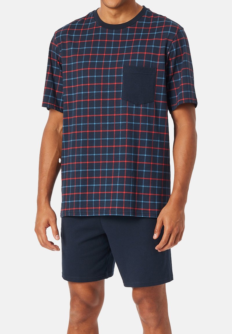 Navy plaid short-sleeve shirt with red and blue grid pattern, featuring a pocket. Paired with dark navy shorts. Cotton blend fabric.