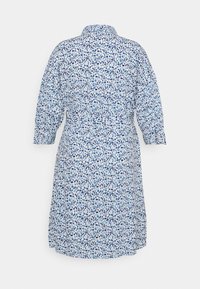 Witte jurk tot op de knie met lange mouwen, blauw onregelmatig stippenpatroon, ceintuur in de taille en kraag, gezien van achteren.