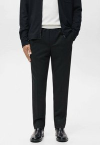 Black wool trousers with a tailored fit, flat front, and side pockets. Paired with a white knit top and a black zip-up jacket.