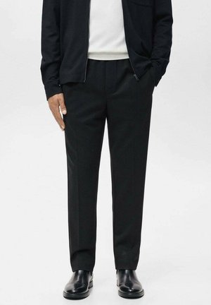 Black wool trousers with a tailored fit, flat front, and side pockets. Paired with a white knit top and a black zip-up jacket.