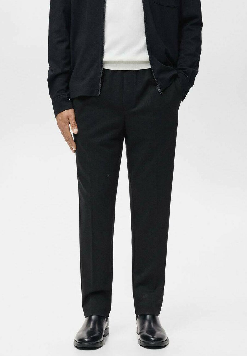 Black wool trousers with a tailored fit, flat front, and side pockets. Paired with a white knit top and a black zip-up jacket.