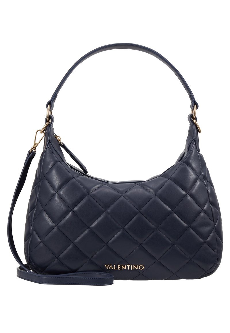 Marinblå quiltad läderhandväska med en enda axelrem och guldhardware. Har ett framträdande varumärkesnamn i guld på framsidan.