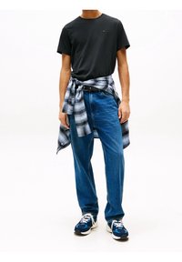 Camiseta de algodón negra, jeans de mezclilla azul claro, camisa de cuadros atada a la cintura y zapatillas azules con acentos blancos. Conjunto casual exhibido.