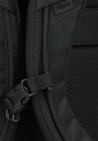 Zwarte nylon rugzak met een gestructureerde stof, verstelbare schouderbanden en een plastic gesp. Bevat een Thule-logo en netdetails.