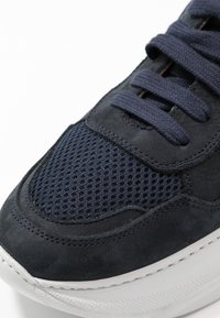 Primo piano della punta di una sneaker blu navy con tessuto a rete, dettagli in pelle scamosciata, lacci abbinati e suola in gomma bianca testurizzata.