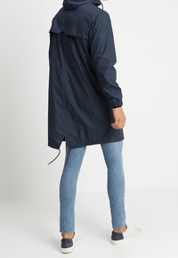 Marinblå vattentät jacka med huva, långa ärmar och elastiska mudd; har en rundad bakre fåll och justerbara dragsko-detaljer.