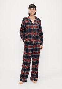 Rød og marineblå plaid pyjamas sæt med en knap-up skjorte, der har en lomme og matchende løstsiddende bukser, prydet med hvid piping.