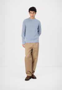 Pull bleu clair côtelé avec un col rond, associé à un pantalon beige à jambes larges et des chaussures marron à enfiler. Tenue simple et décontractée.