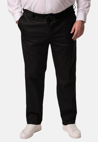 Zwarte broek met een trekkoord in de taille, met een zachte structuur en een taps toelopende snit, gecombineerd met witte sneakers.