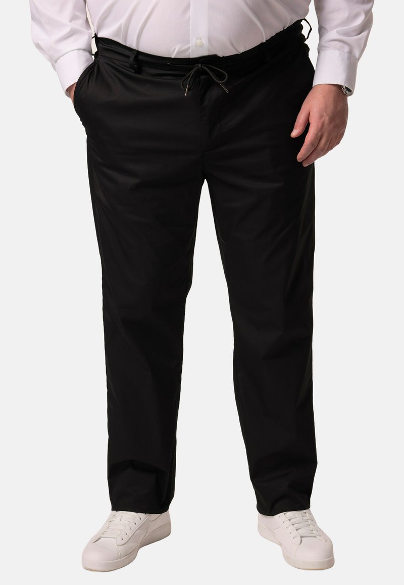 Zwarte broek met een trekkoord in de taille, met een zachte structuur en een taps toelopende snit, gecombineerd met witte sneakers.