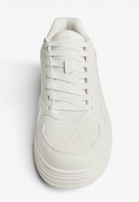 Bijela atletska cipela od glatke kože s reljefnim mrežastim jezikom, ravnim vezicama, perforiranim vrhom za prozračivanje i slojevitim dizajnom potplata.