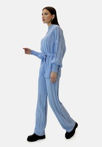 Jasnoniebieski dwuczęściowy zestaw dzianinowy z fakturą prążkowaną, długimi rękawami i paskiem w talii. Dopełniony czarnymi butami na platformie.