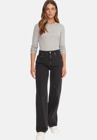 Jeans neri a vita alta con vestibilità a gamba dritta, realizzati in denim dalla texture morbida. Abbinati a una maglia aderente a maniche lunghe di colore grigio chiaro.