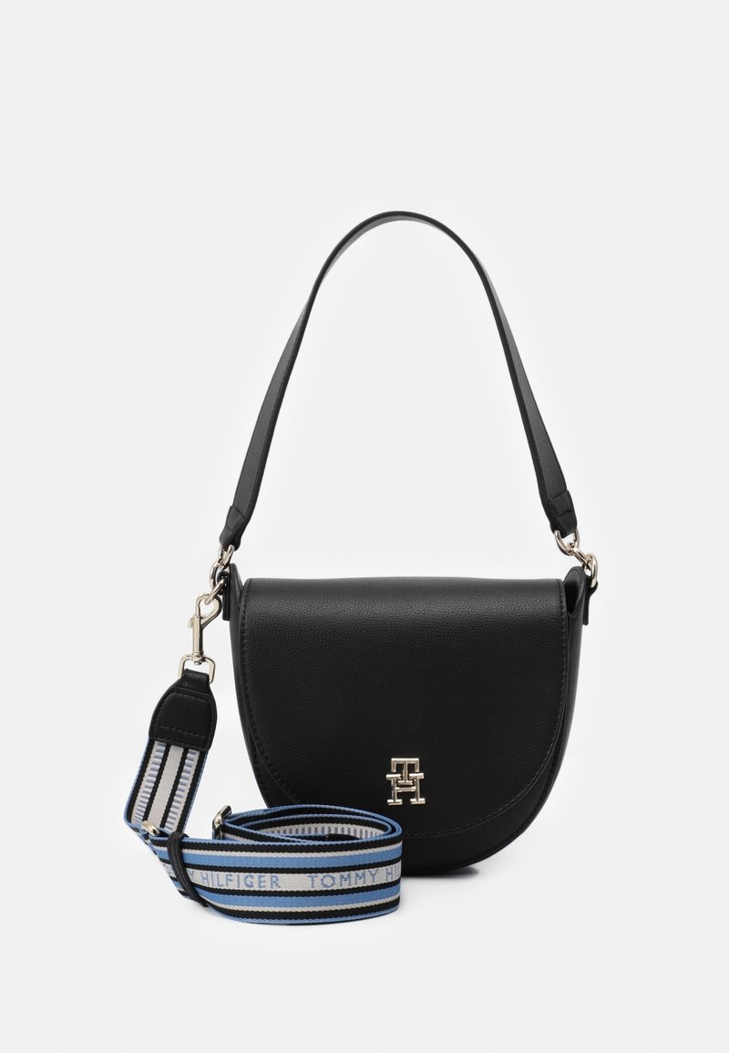 Sac bandoulière en cuir noir avec rabat incurvé, petit logo doré à l'avant et une bandoulière en tissu rayé bleu, blanc et noir amovible.