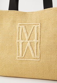 Geweven rieten draagtas in lichtbeige met een gestructureerde afwerking. Voorzien van een verhoogd logo in bijpassend materiaal en zwarte stoffen handvatten.