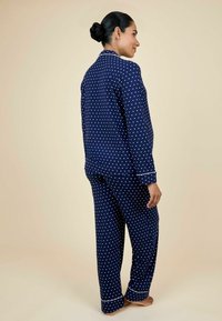 Námornícky modrý pyžamový set s bodkami, ktorý obsahuje košeľu s gombíkmi a golierom a zodpovedajúce nohavice, oboje s bielym lemovaním a jemnou textúrou.