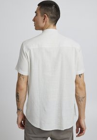 Chemise blanche à manches courtes en lin léger, avec un ourlet arrondi et un design simple à l'arrière. Longueur à la taille avec une coupe décontractée.