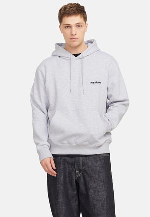 Grauer Kapuzenpulli mit Kordelzügen, Fronttasche und Logo auf der Brust. Getragen über dunklen Jeanshosen, mit gerippten Bündchen und Saum.