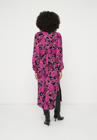 Dolga obleka v živahnem rožnatem cvetličnem vzorcu na črnem ozadju, z zatisnjenim pasom in stranskimi razporki. V kombinaciji z črnimi škornji do kolen.