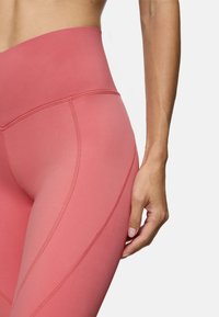 Legginsy z wysokim stanem, wykonane z miękkiego, lekkiego, różowego materiału, z bezszwowym projektem i subtelnymi ukośnymi przeszyciami.