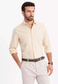 Helles beiges Button-Up-Hemd mit hochgekrempelten Ärmeln, kombiniert mit hellen Hosen und einem schwarzen Gürtel. Glatte Textur, klassisches Kragendesign.