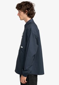 Navyblauwe shirt met een kraag, elastische manchetten en een zak aan de voorkant. Gemaakt van lichtgewicht stof, met een relaxed fit.