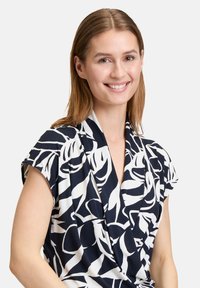 Blusa blu navy con motivo floreale bianco, maniche corte e scollatura a V. Realizzata in tessuto leggero con una texture liscia.