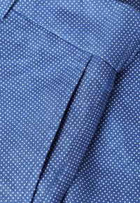 Gros plan d’un tissu bleu avec un petit motif à pois blancs, montrant des coutures détaillées et une couture pliée.