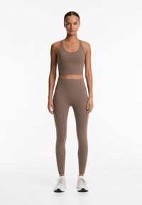 Braunes sportliches Crop-Top und hochgeschnittene Leggings, gefertigt aus dehnbarem Stoff mit nahtloser Verarbeitung und subtilen Nähdetails.