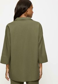 Olive green oversize koszula z teksturowanej tkaniny, z klasycznym kołnierzykiem, szerokimi rękawami trzyczwartkowymi i prostym dołem.