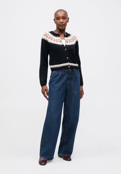 Cárdigan navy con un yugo ligeramente estampado, botones dorados y dobladillo acanalado, combinado con jeans de mezclilla azul de pierna ancha.