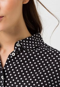 Svart knapp-up skjorta med vita prickar, med en klassisk krage och en strukturerad tygkvalitet. Inkluderar sydda knappar och en slät yta.