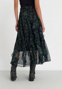 Zwarte rok met groen bloemenpatroon, gelaagd ontwerp, gerimpelde zoom en elastische tailleband, gecombineerd met zwarte laarzen tot over de knie.