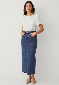 Hvid, top med hulmønster og korte ærmer, parret med en højhalset, lang denimnederdel i mørkeblå, afsluttet med en frynset kant.