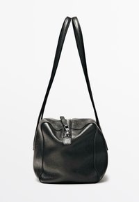 Sac à main en cuir noir texturé avec une fermeture éclair supérieure et deux longues lanières, présenté sur un fond blanc uni.