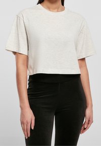 Przycięty, jasnobeżowy t-shirt z okrągłym dekoltem i krótkimi rękawami. Miękka tkanina o subtelnej fakturze. W połączeniu z czarnymi prążkowanymi legginsami.