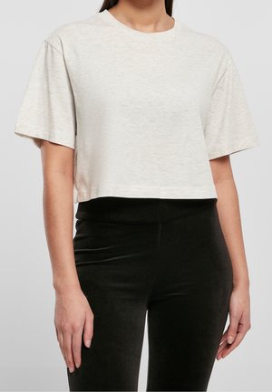 Avskuren, ljusbeige t-shirt med rund halsringning och korta ärmar. Mjuk tyg med en subtil textur. Kombination med svarta ribbade leggings.