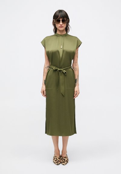 Olive green midi dress with short cap sleeves, tie waist, side slits, and a round neckline, paired with leopard print slip-on shoes.