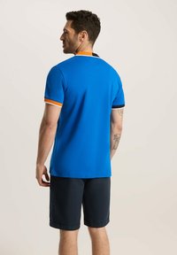 Niebieska koszulka polo z pomarańczowymi i czarnymi akcentami na kołnierzyku, krótkie rękawy oraz granatowe szorty; materiał wydaje się gładki z dopasowanym krojem.