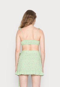 Top de cropped floral verde com alças ajustáveis e saia mini com babados. O tecido é leve, com uma estampa floral dispersa em rosa e amarelo.