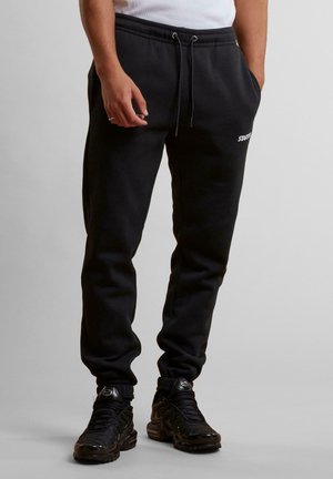 Sorte sweatpants lavet af blødt materiale, med en afslappet pasform, elastisk snøre i taljen og logo detaljer på låret. Paired med sorte sportssko.