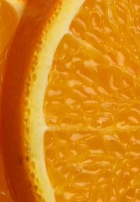 Skivad apelsin som visar det ljusa orange köttet, en texturerad yta och en kontrasterande ljusgul skal med synliga saftdroppar.