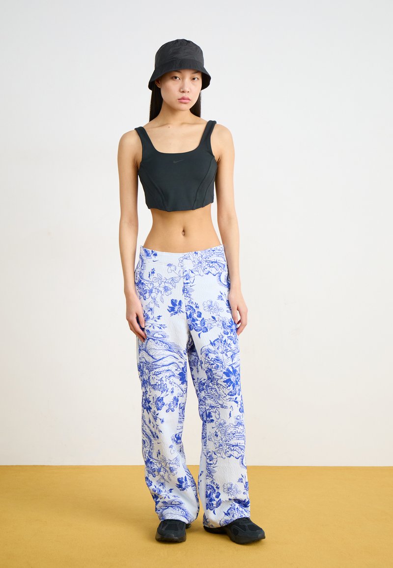 Zwarte crop top met brede banden en losse blauwe broek met een patroontje in bloemen. Gestyled met een zwarte bucket hat en eenvoudige zwarte schoenen.