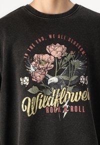 Sudadera negra con cuello redondo, con gráficos florales y de águila, y el texto "Wildflower Rock & Roll" en amarillo y rosa.