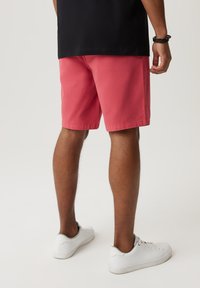 Czerwone szorty wykonane z bawełny, o regularnym kroju i wykończonych brzegach, w zestawie z białymi trampkami na neutralnym tle.