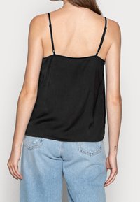 Camisola nera con spalline regolabili, texture liscia e vestibilità ampia, abbinata a jeans in denim azzurro chiaro con dettagli strappati.