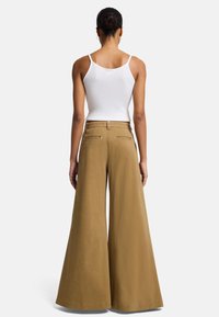 Pantaloni khaki a gamba larga con vita alta, realizzati in un tessuto morbido. Presentano tasche posteriori classiche e un design pulito e semplice.