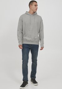 Sudadera con capucha gris y un bolsillo frontal, con una tela texturizada y cordones ajustables. Combinada con jeans azul oscuro y zapatillas negras.