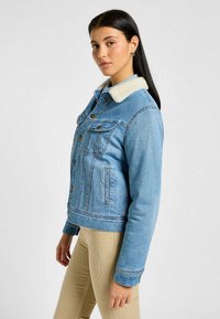 Chaqueta de mezclilla azul claro con cuello de borrego, cierre frontal de botones, bolsillos en el pecho y bolsillos laterales, con un diseño corto y mangas largas.